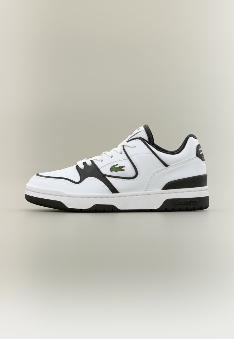 Λευκό χαμηλό αθλητικό παπούτσι με μαύρες λεπτομέρειες, λευκά κορδόνια και πράσινο λογότυπο κροκόδειλου στο πλάι, σε ουδέτερο φόντο.