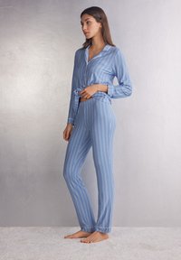Blue gestreepte pyjama set van zachte stof. Het topje heeft een kraag en een knoopdetail, terwijl de broek een elastieken tailleband en omgeslagen boorden heeft.