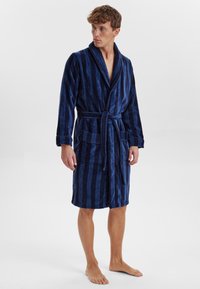 Accappatoio a righe navy realizzato in morbido cotone felpato. Presenta un colletto a scialle, una vita con lacci e due tasche anteriori. Design alla lunghezza del ginocchio.
