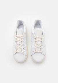 Zapatillas blancas de cuero con textura suave, puntera redonda, detalles perforados y cordones en crema, con una suela de goma beige.