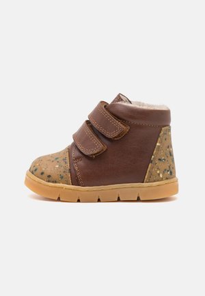 Bottines en cuir marron avec deux bandes Velcro, embout tacheté beigne, doublure douce et semelle en caoutchouc beige avec des rainures pour une traction optimale.