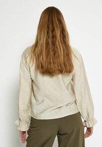 Light beige long-sleeve blouse with textured fabric featuring a square pattern. Gathered sleeves and a loose fit provide a relaxed silhouette.