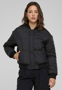 Černá vycpaná bomber bunda s kulatým výstřihem, předním zipem, elastickými manžetami a bočními kapsami. Texturovaná tkanina s prošívaným designem.