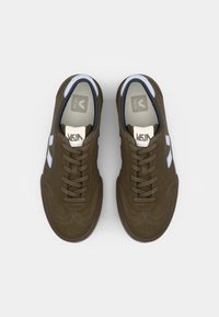 Sapatilhas castanhas com acabamento liso e detalhes brancos, apresentando um design de atacadores tradicional e bico arredondado. Sola cinza visível.