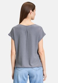 Blusa a maniche corte blu navy con motivo a pois e piega sul retro; tessuto leggero; vestibilità rilassata e orlo curvo.