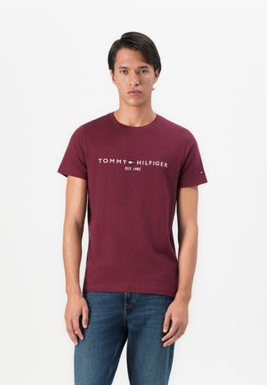 Burgundska pamučna majica s kratkim rukavima koja sadrži logo "TOMMY HILFIGER EST. 1985" u bijeloj boji, okrugli izrez i glatku teksturu.