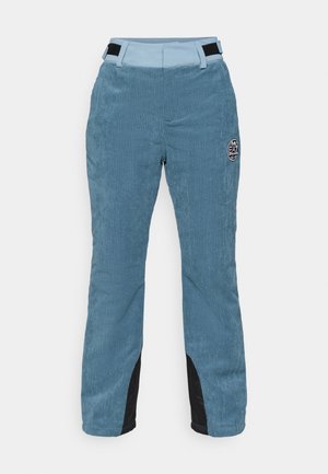 Pantaloni din catifea albastră, cu croială dreaptă, având un accent negru pe părțile inferioare și o etichetă rotundă cu logo-ul EA pe față.