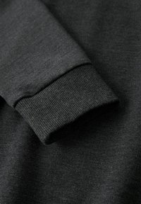 Dunkelgrauer Sweatshirtärmel mit geripptem Bündchen, nah aufgenommen, um die Stoffstruktur und Nähdetails hervorzuheben.