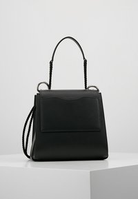 Musta nahkainen käsilaukku, jossa on yläkahva ja kierretty köysihihna, esillä valkoisella jalustalla yksinkertaista taustaa vasten.