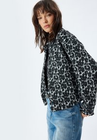 Giacca a stampa leopardata in bianco e nero con vestibilità comoda, chiusura a bottoni e tessuto testurizzato, abbinata a jeans in denim blu.