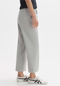 Pantalons fuselés gris clair avec une texture lisse, poches latérales et ceinture élastique. Portés avec des baskets blanches avec des accents noirs.