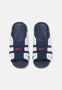 Tamsiai mėlynos šlepetės su baltomis petnešomis, raudonu Nike logotipu, perforuotu dizainu ir tekstūruota padas, kuris suteikia sukibimą. Dvi reguliuojamos petnešos su sagtimis.