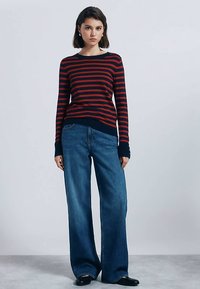 Rood en marineblauw gestreepte trui met een ronde halslijn, gecombineerd met wijde blauwe spijkerbroeken. Gladde textuur en een aansluitend ontwerp bij de taille.