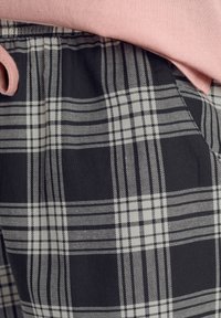 Black and white plaid patterned fabric with a smooth texture; a pink sweatshirt overlaps the waistband, adding a contrasting color.
