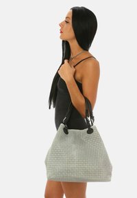 Grå vävd handväska med texturerad yta, försedd med svarta läderhandtag och runt beslag. Strukturerad form, rymlig design.