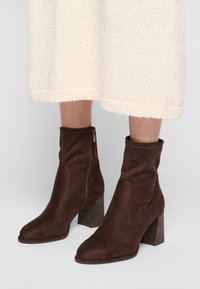 Bottines en daim marron avec une texture lisse, dotées d'une fermeture éclair sur le côté et d'un talon carré à motifs.