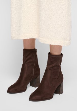 Stivali alla caviglia in suede marrone con una consistenza liscia, dotati di una zip laterale e di un tacco a blocco quadrato e decorato.