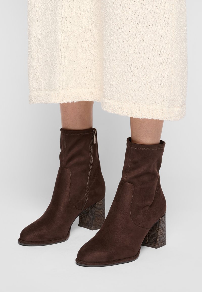 Bottines en daim marron avec une texture lisse, dotées d'une fermeture éclair sur le côté et d'un talon carré à motifs.