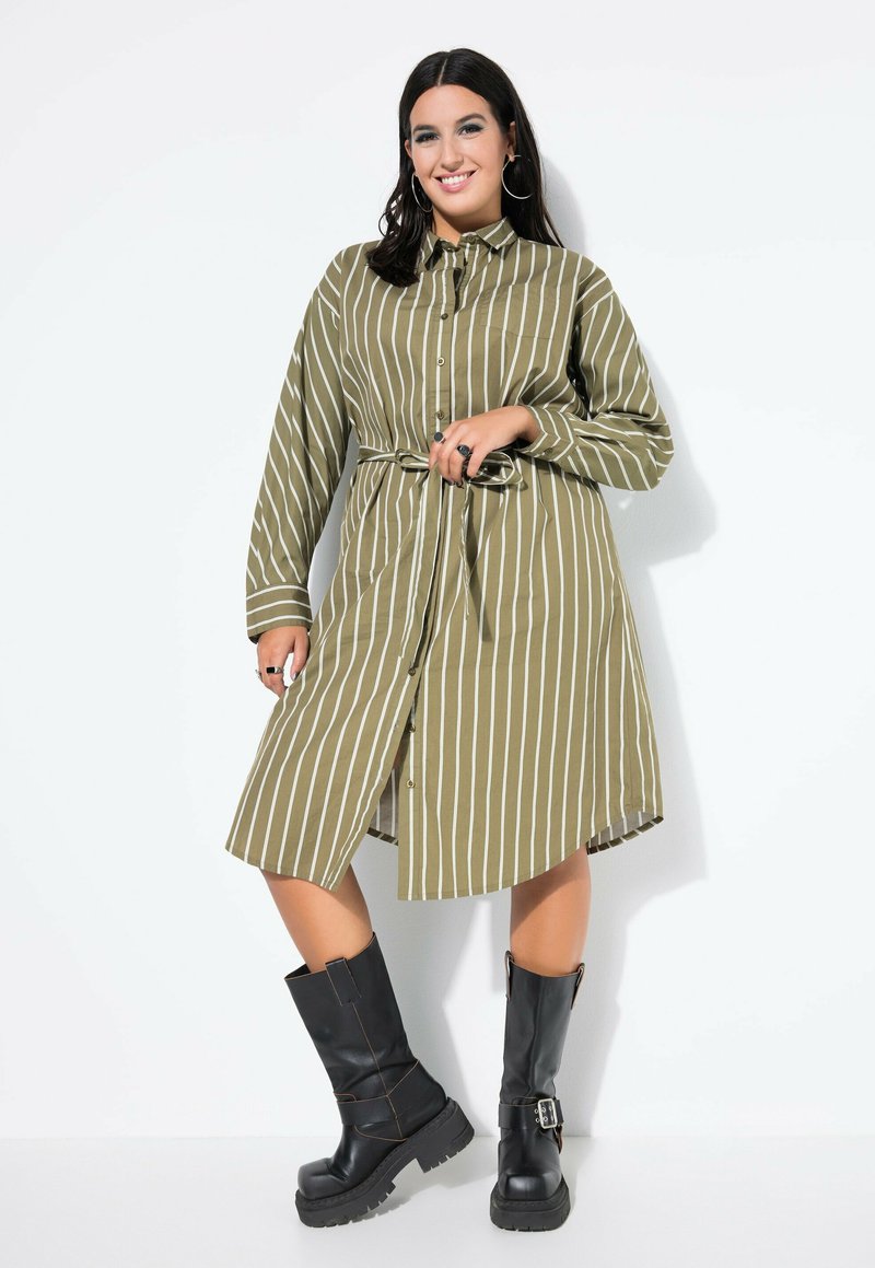 Dunkelgrün gestreift, kurzärmliges Kleid mit langen Ärmeln, Gürtel in der Taille und knielanger Säume, kombiniert mit schwarzen klobigen Stiefeln mit Absatz.