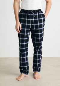 Mustat ruudulliset pyjamahousut, joissa on valkoinen ruutukuosi, joustava vyötärö, naru ja sivutaskut. Pehmeä kangas, rento malli.