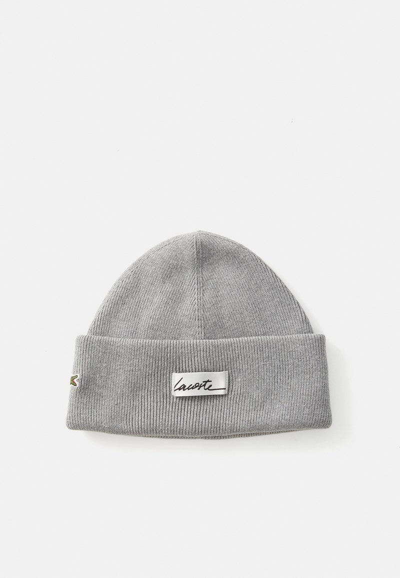 Grå strikket beanie med foldet kant, der har et struktureret ribbet mønster og et Lacoste-label syet på forsiden.