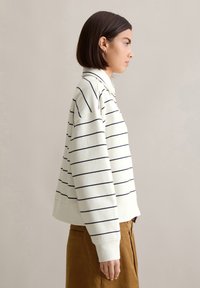 Wit en marineblauwe gestreepte sweatshirt met een kraag, een cropped ontwerp en brede mouwen. Draagt een paar bruine corduroybroek.