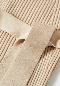 Tissu en beige côtelé avec une texture lisse, featuring une large bande plate et un détail de nouage, le tout dans une teinte douce et neutre.