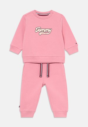 Rožinė sportinė palaidinė su "Tommy" logotipu, apvalia iškirpte ir spaudimo mygtukais. Derančios rožinės sportinės kelnės su juostele ir gumburu, bei stangriomis rankovėmis.