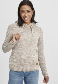 Beige strikket genser med hette, med treknapper og et teksturert mønster. Merke på nedre høyre hjørne.