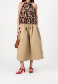 Luipaardprint haltertop met ruffles, beige geplooide midi-rok, rode open-toe hakken met zilveren accenten en een bruine schoudertas.