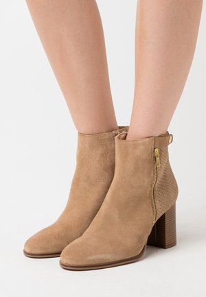 Bottines en suède beige avec un côté texturé, fermeture à glissière dorée et un talon en bois empilé. Design à bout pointu.
