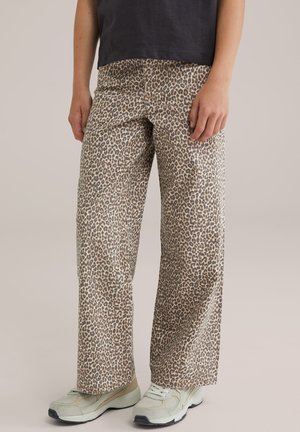 Leopardenmuster-Hosen aus gewebtem Stoff, im lockeren Schnitt und mit weitem Bein, kombiniert mit hellen Sneakers.