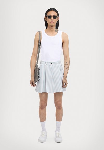 Balta tank top, gai zila svārku apakšdaļa ar krokām, pelēka soma un baltas sporta kurpes. Modelis valkā saulesbrilles un baltas zeķes.
