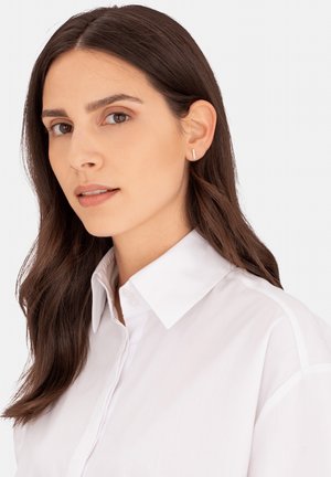 Weißes Hemd mit Kragen, das über einen Knopfverschluss verfügt und eine glatte Textur aufweist. Das Model trägt einen schlichten silbernen Ohrring. Die Haare sind braun und wellig.
