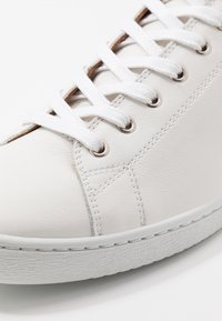 Baskets en cuir blanc avec bout rond, lacets blancs, œillets métalliques et semelle en caoutchouc texturée. Présentent des coutures contrastées et un design épuré.