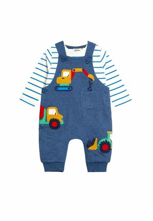 Blaue Baby-Latzhosen mit aufgenähten Baustellenfahrzeugen, getragen über einem weißen Langarmshirt mit blauen Streifen.