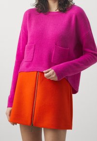 Fuchsia Strickpullover mit zwei Fronttaschen, kombiniert mit einem orangenen A-Linien-Rock mit einem zentralen Reißverschluss. Weicher Textur, modernes Design.