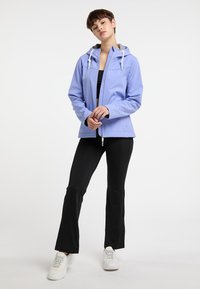 Giacca impermeabile lilla con cappuccio, cordini bianchi e un discreto logo a forma di cuore. Abbinata a pantaloni neri e sneakers bianche.