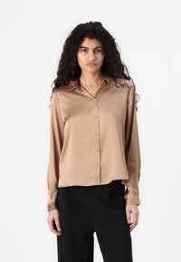 Bruine satijnen blouse met lange mouwen en een knopenlijst aan de voorkant en kraag, met een iets cropped ontwerp en een zachte glanzende textuur.
