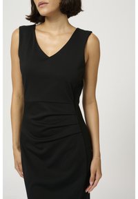 Robe noire sans manches avec un décolleté en V, présentant un tissu froncé à l'avant et des détails côtelés sur les côtés. Texture lisse.