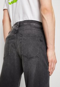 Mörkgrå denimjeans med en klassisk femficksdesign, som har subtil blekning och en slät textur, visad bakifrån.