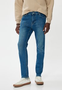 Vaqueros de denim azul con un ajuste de pierna recta, diseño de cinco bolsillos, ligero desvanecimiento y cierre de botón de latón. Combinados con zapatillas color crema.
