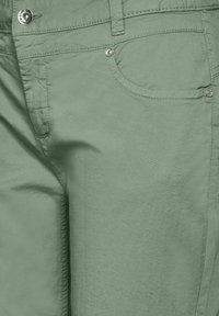 Vihreät puuvillaiset housut, joissa on sileä pinta, etutasku ja hopeinen nappi vyötäröllä.