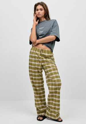 Szary, oversize t-shirt z białym napisem, w połączeniu z luźnymi oliwkowymi spodniami w kratę, posiadającymi elastyczny pas i sznurek do regulacji. Czarne klapki.