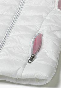 Vit vadderad jacka med glansig yta, med en central dragkedja och en sidoficka med rosa foder. Metallisk dragkedjeskyttel med hjärtformad detalj.