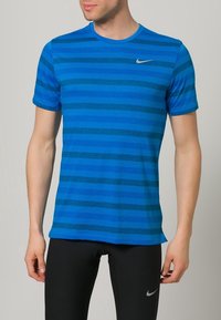 Sininen lyhythihainen T-paita, jossa on vaakasuoria raitoja vaihtelevissa sävyissä. Valmistettu kevyestä materiaalista; siinä on pieni hopeinen Nike-logo rinnassa.