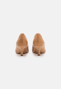Chaussures à talons hauts en cuir beige avec un bout arrondi et un talon fin. Texture lisse et design minimaliste avec des détails de coutures visibles.