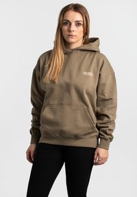 Khaki mikina s kapucňou vyrobená z mäkkej, textúrovanej látky. Obsahuje veľkú prednú kapsu a rebrované manžety. Minimalistické logo v svetlejšej farbe.