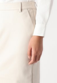 Beige leren rok met een gladde textuur, voorzien van een platte tailleband en zijzakken, gecombineerd met een witte blouse met knopen.