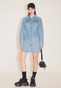 Ruoshu denim valkoisena pitkähihaisen mekon, jossa on edessä napit, kaksi rintataskua ja rento leikkaus. Yhdistetty mustiin paksupohjaisiin lenkkareihin ja pieneen mustaan laukkuun.
